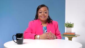 A professional woman with expertly styled hair and makeup smiles with confidence for the camera at her desk for a branding photoshoot.
